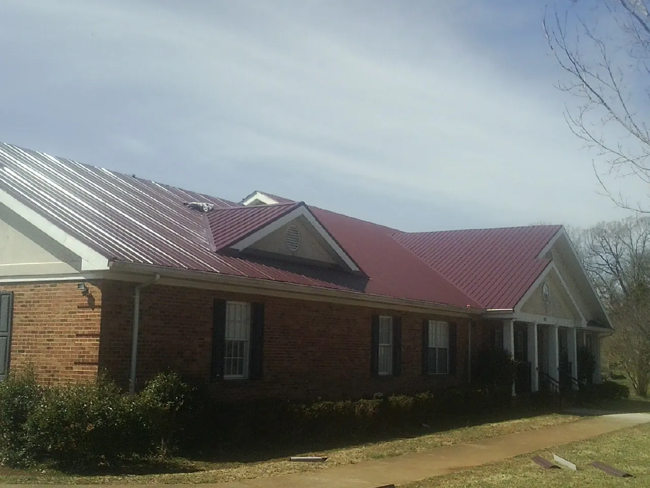 Red metal roof with gabled entries on a long brick building, from a Hail Damage Roof Repair job in Waynesboro