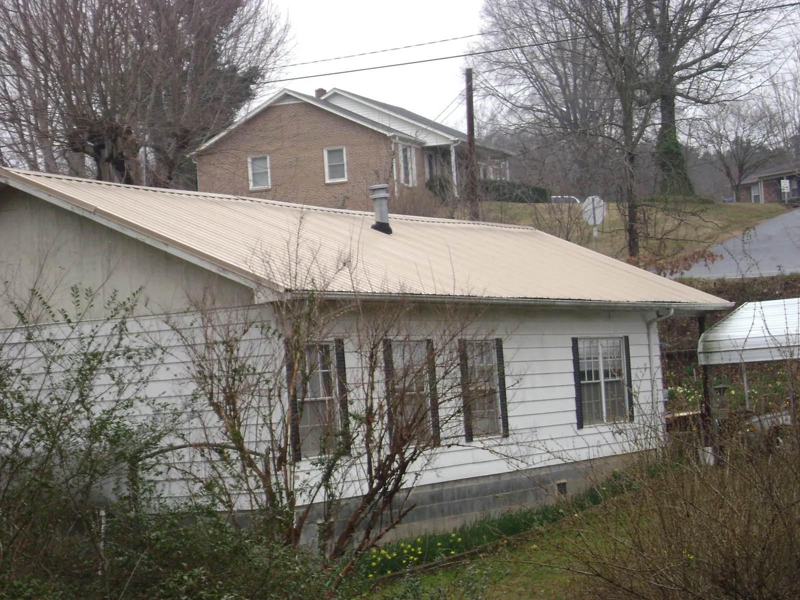 Tan metal roof on a white sided house set into a hillside — Commercial Roofing by Roofing Brothers in Waynesboro